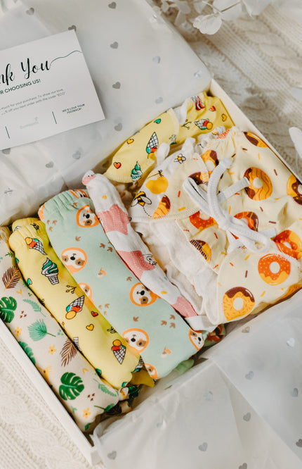 Eco-friendly baby shower gift box with reusable cloth diapers and colorful muslin nappies displayed on a soft beige blanket.