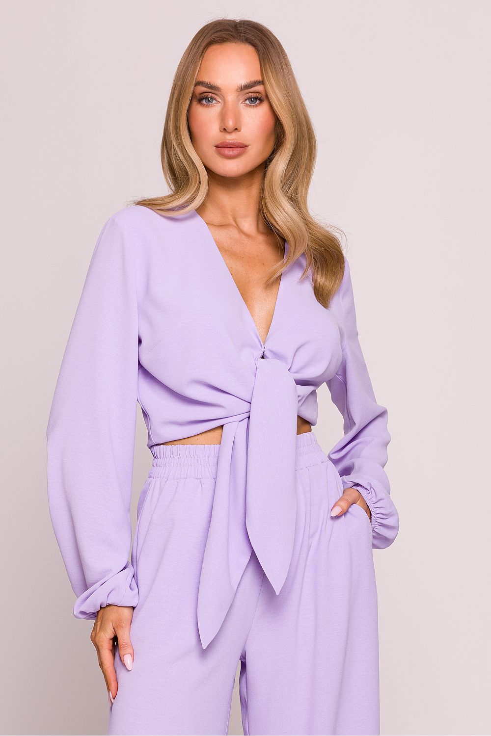 Woman wearing a stylish two-piece crepe set with a deep V-neck crop blouse and high-waisted wide-leg pants. The blouse features long puff sleeves and a tie front detail. Lightweight fabric with a matte finish, ideal for spring and summer. Elegant and comfortable outfit designed for women seeking timeless style with a modern twist. Perfect for brunch, travel, or casual occasions.